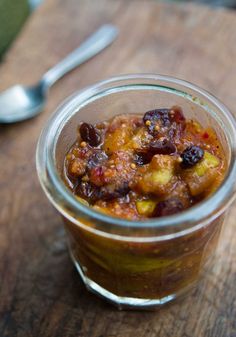 a glass jar filled with food sitting on top of a wooden table next to a spoon