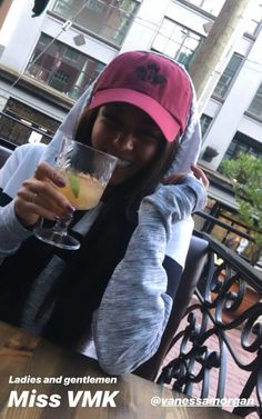 a woman wearing a pink hat and holding a wine glass in her hand while sitting at a table