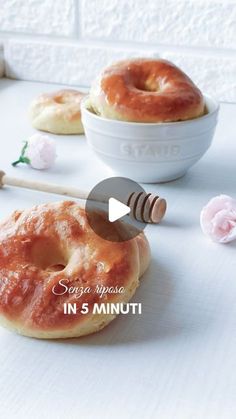 two glazed donuts sitting on top of a table next to a bowl of doughnuts