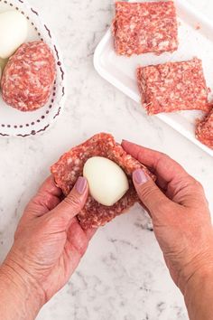 a person holding an egg in their hand near some meat patties on a plate