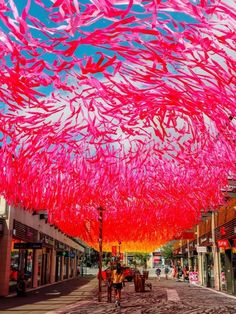 an artistic display of pink streamers hanging from the ceiling in front of shops on a city street