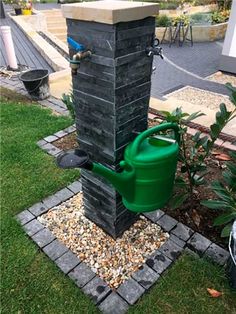 a large green watering can sitting next to a brick fire hydrant