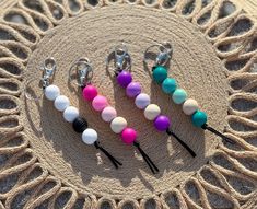 four different colored beads and black hooks on a piece of rope with a circular doily in the background