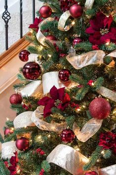 a decorated christmas tree with red and gold ornaments on it's branches in front of a banister