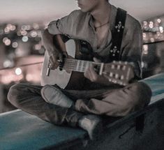 a man sitting on top of a roof playing a guitar