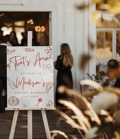 a sign that is sitting on a wooden easel in front of a building with people standing around it