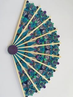 a fan made out of matchesticks and beads on a white surface with a purple center