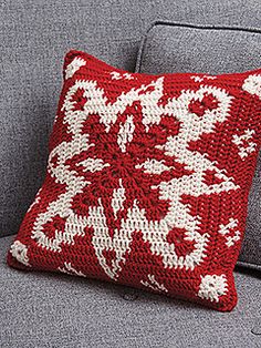 a red and white knitted pillow sitting on top of a gray couch next to a laptop