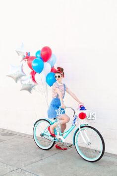 a woman riding a bike with balloons on the front and back wheel, wearing patriotic clothing