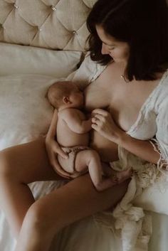 a woman is holding a baby in her lap while laying on a bed with white sheets