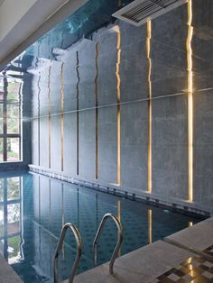 an indoor swimming pool with stairs leading up to the water's edge and windows above it