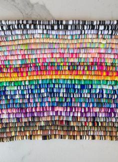 a multicolored wall hanging made out of different colored paper strips on a marble surface