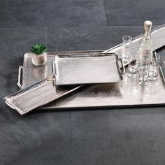 a silver tray with glasses and bottles on it sitting on the floor next to a potted plant