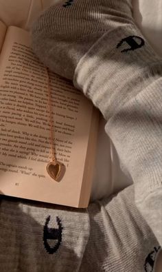 an open book with a gold heart on it laying on a bed next to some socks