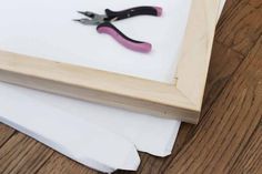 a pair of pink scissors sitting on top of a piece of paper next to a wooden frame