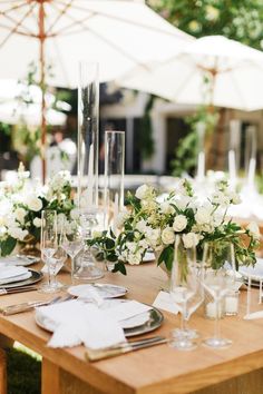 a long table with white flowers and greenery is set for an outdoor wedding reception