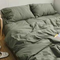 an unmade bed with green sheets and pillows on the floor next to a lamp