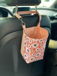 an orange and white flowered purse hanging from the back of a car seat in a vehicle