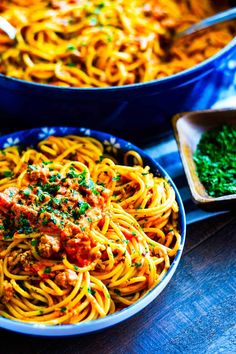 two blue bowls filled with spaghetti and meat on top of a wooden table next to other dishes