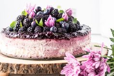 a cake with blueberries and blackberries on top sitting on a wooden table next to purple flowers