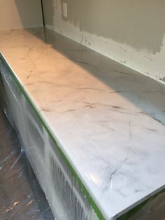 a white counter top with green tape on the bottom and one piece of plastic wrapped around it