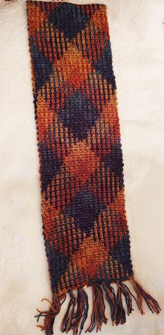 an orange, black and brown scarf laying on top of a white furnishing