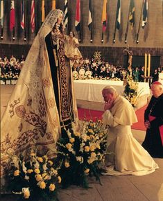 the pope is kneeling down in front of a floral arrangement with flowers and candles on it