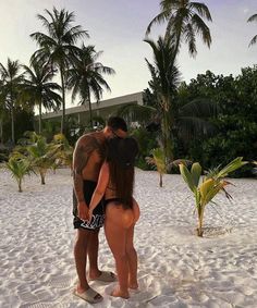 two people standing in the sand with palm trees behind them and one person wearing a black swimsuit