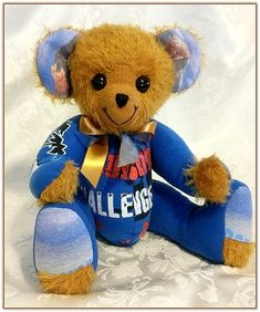 a brown teddy bear sitting on top of a white bed covered in blue and gold