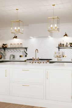 a kitchen with white cabinets and gold accents on the counter tops, along with hanging lights