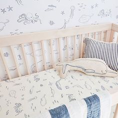 a baby crib with blue and white wallpaper in the background, along with an ocean themed pillow