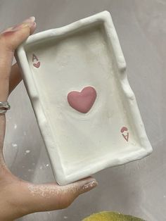 a hand holding a small white square plate with hearts on it and two lemons next to it