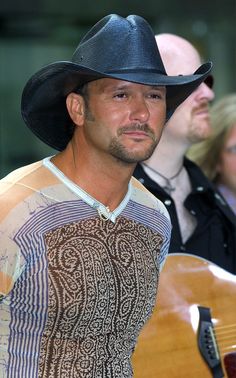 a man wearing a cowboy hat and holding an acoustic guitar in front of other people