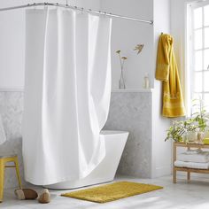 a white bathroom with yellow accents and towels on the shower curtain, rugs and bathtub