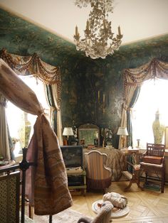 the room is decorated in green and gold with chairs, chandelier, rugs, and curtains