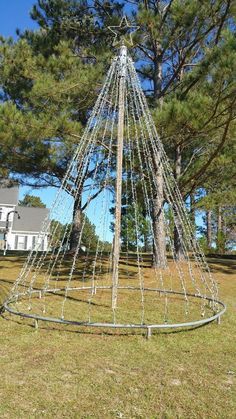 a large metal structure sitting in the middle of a field next to a house and trees