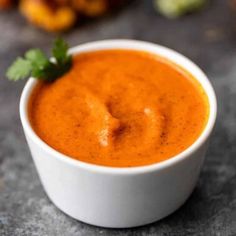 a small white bowl filled with sauce and garnished with cilantro leaves