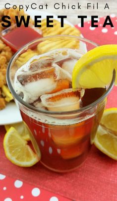 a glass filled with ice and some lemon wedges on top of a red table