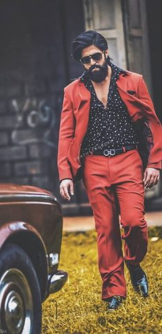 a man in red pants and a black shirt is standing next to an old car