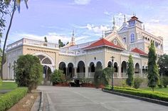 a large white building surrounded by lush green trees and shrubbery in front of it