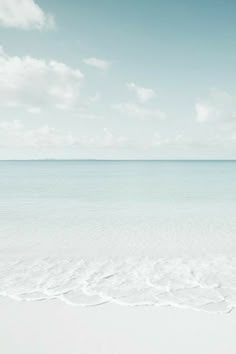 an empty beach with white sand and blue water in the distance, under a partly cloudy sky