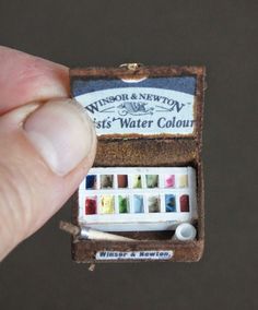 a miniature box with watercolors in it being held by a person's hand