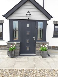 two flower pots with tulips in front of a gray door on a white house