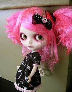 a doll with pink hair and big eyes wearing a black dress is standing next to a wall