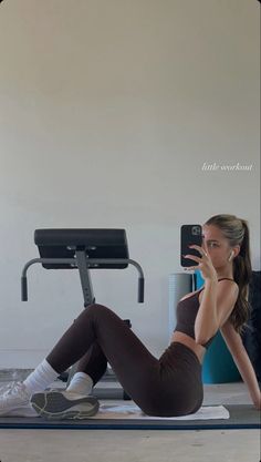 a woman is sitting on the floor talking on her cell phone while doing exercises in front of a treadmill