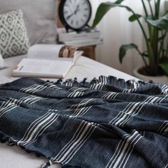 the blanket is laying on top of the bed next to an open book and clock