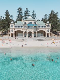 people are swimming in the clear blue water near a large white building with many balconies