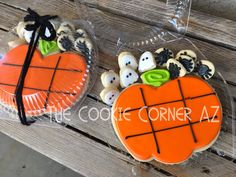 two decorated cookies in the shape of pumpkins on top of a wooden bench with black ribbon