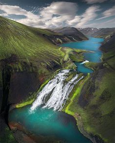 an aerial view of a waterfall in the middle of a green valley with blue water