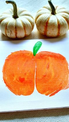 an orange painted on paper next to two small pumpkins